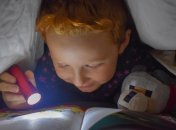 Ребенок читает при свете фонарика