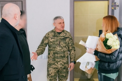 Олег Іващенко у військовій формі з годинником на лівому зап’ясті розмовляє з людьми, поруч жінка з букетом