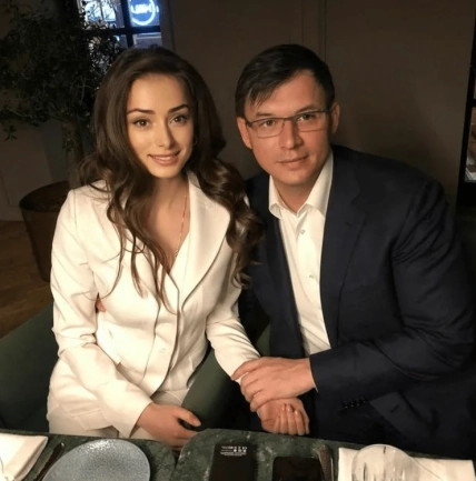 Мужчина в темном костюме и женщина в белом жакете сидят за столом