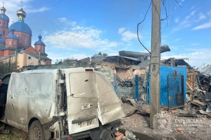 Пошкоджений білий фургон перед зруйнованою будівлею; поруч церква та бетонний стовп