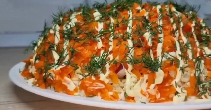 Слоеный салат с тертой морковью, майонезом и укропом на белой тарелке