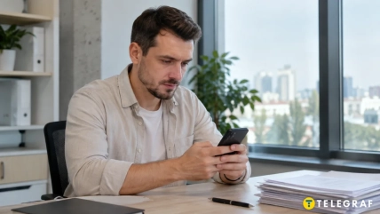 Чоловік дивиться на смартфон, сидячи за столом із документами