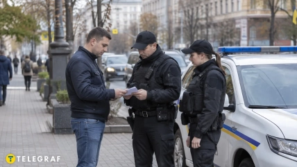 Мужчина показывает документы двум полицейским возле служебного автомобиля