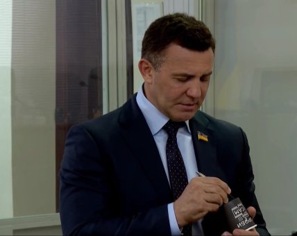 Николай Тищенко во время заседания ВАКС об избрании ему меры пресечения дарит журналистам свой автограф на пустом стаканчике. Скриншот видео "Общественного" из зала суда