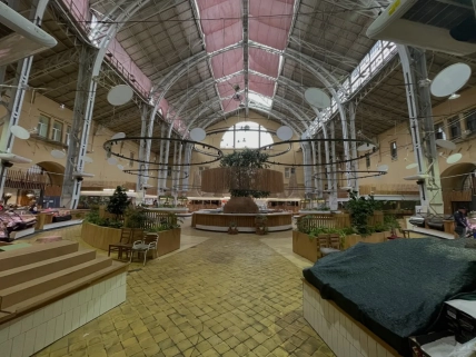 Пустой зал рынка с торговыми прилавками, деревянными ограждениями с растениями и высоким металлическим потолком