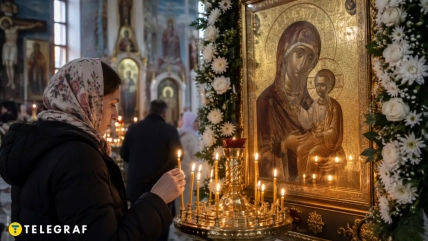 Женщина в платке ставит свечу перед украшенной цветами иконой Богородицы с младенцем