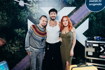 Двое мужчин и рыжеволосая женщина позируют на фоне логотипов SWEET.TV Originals и Destination X