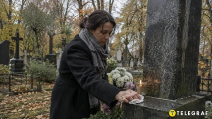 Женщина вытирает надгробие на кладбище возле цветов и зажженной свечи