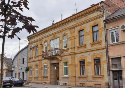 Жовта двоповерхова цегляна будівля з декоративним фасадом і балконом на міській вулиці