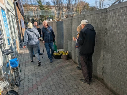 Люди біля магазинів у вузькому проході поруч із захисною огорожею та ящиками з фруктами