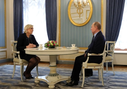 Марин Ле Пен и Владимир Путин сидят за столом в зале с украшенными стенами