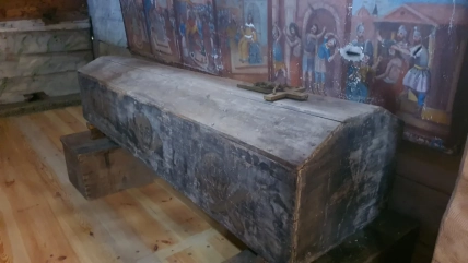 Старинна закрита дерев’яна труна з хрестом на кришці стоїть біля стіни з релігійними розписами
