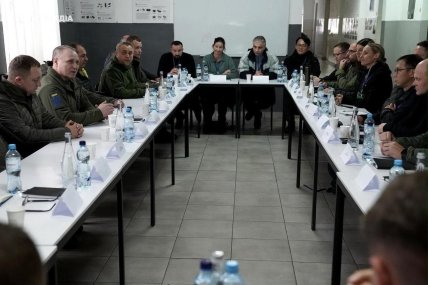 Військові та цивільні учасники зустрічі сидять за столами у формі літери П