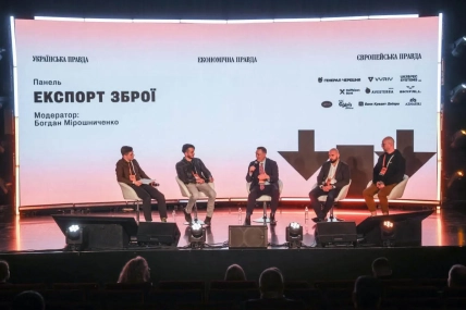 П’ятеро чоловіків сидять на сцені перед екраном із написом "Експорт зброї"
