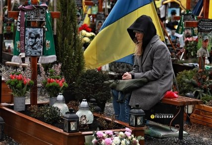 Женщина сидит у могилы защитника.