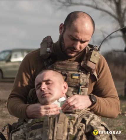 Чоловік у військовому спорядженні надає допомогу пораненому бійцю