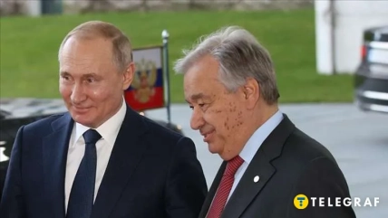 Антоніу Ґутерриш та Володимир Путін у темних костюмах стоять поруч, позаду видно прапор Росії