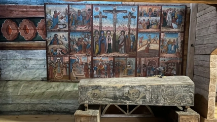 Дерев’яна труна із зображеннями черепів стоїть перед стіною з релігійними розписами