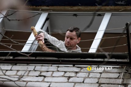 Чоловік змітає сміття з балкона після влучання ракети поруч