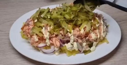 Слоеный салат с рыбой, маринованными огурцами и красным луком на белой тарелке