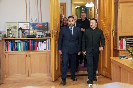 Зеленський і чоловік у костюмі виходять із кімнати, позаду них у дверях стоїть високий охоронець у чорному