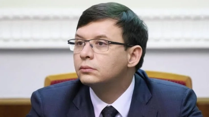 Мужчина в очках и темном костюме сидит за столом