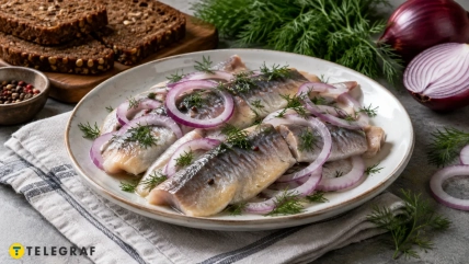 Филе сельди с кольцами красного лука и укропом на тарелке, рядом ржаной хлеб