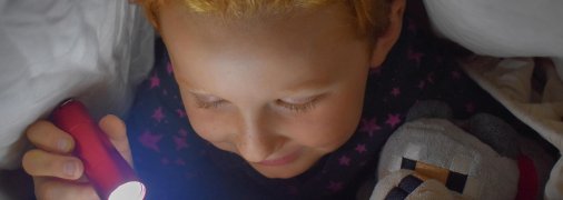 Дитина читає при світлі ліхтарика